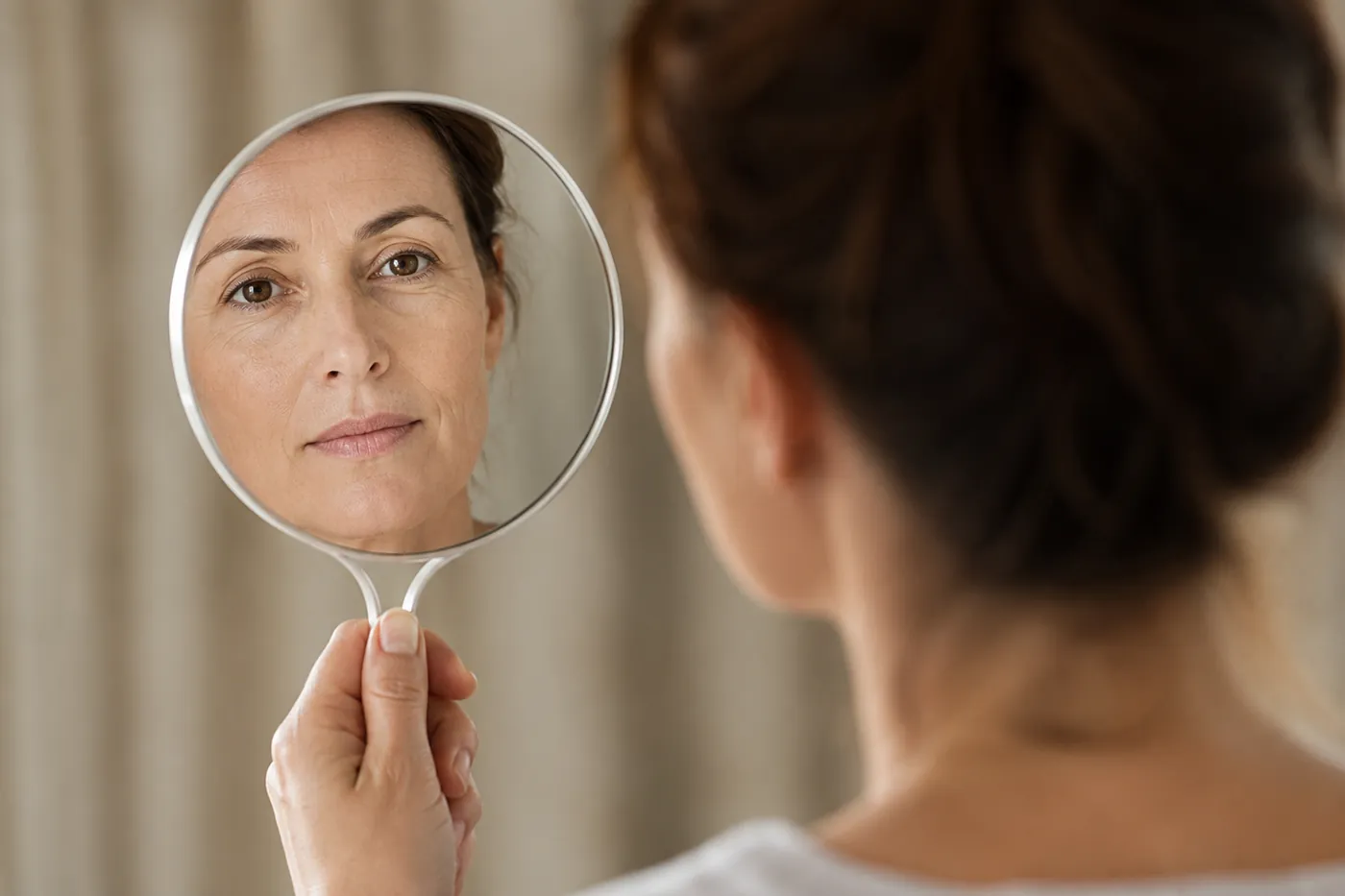 Mujer mirándose en un espejo de mano mientras valora una blefaroplastia